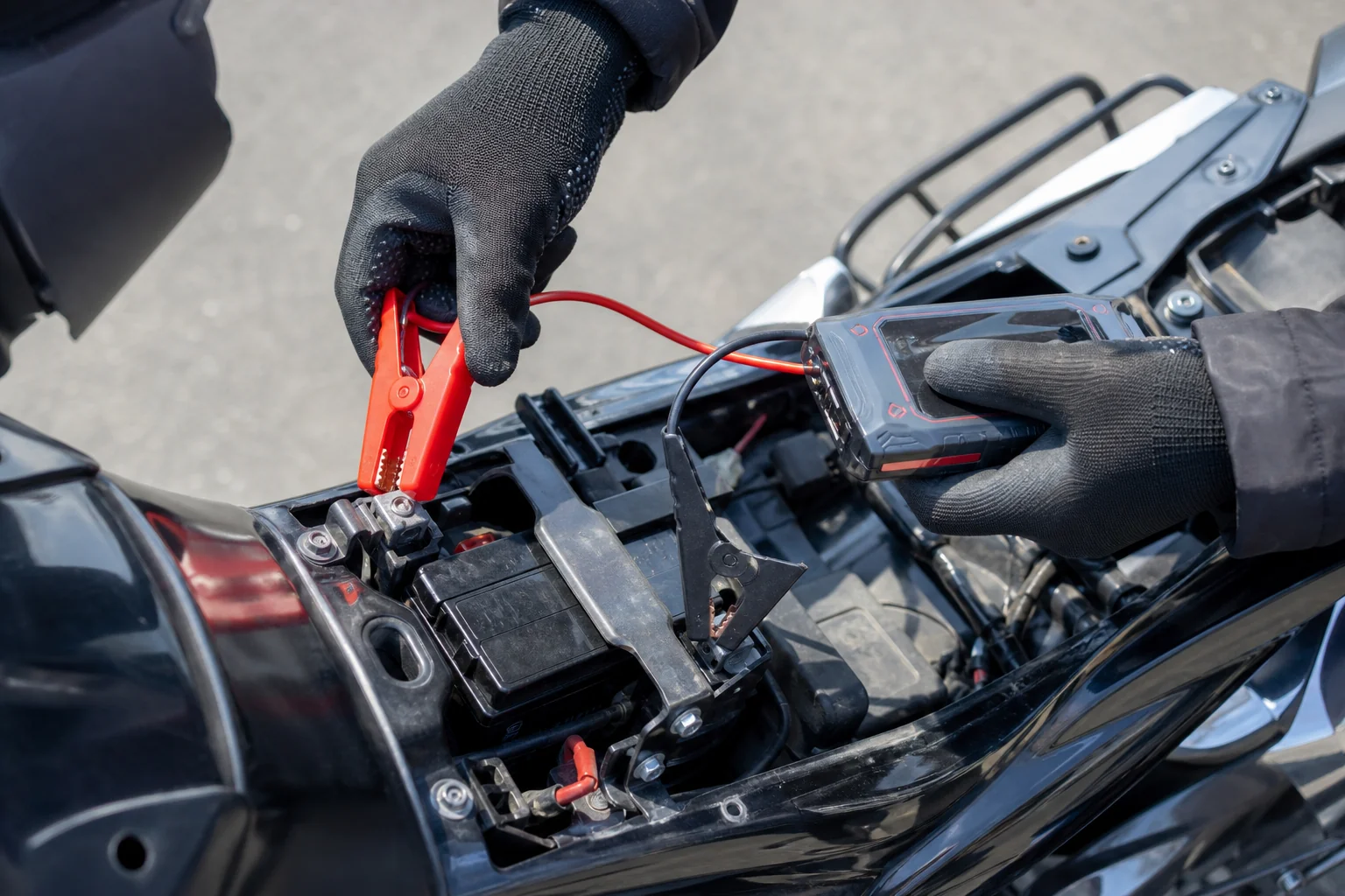 シートを外したバイクのバッテリーにジャンプスターターのクリップをつなぐ手元